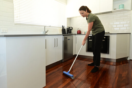 Adult Woman Suffering From Compulsive Cleaning Disorder Using A Broom, Sweeping A Home Kitchen.