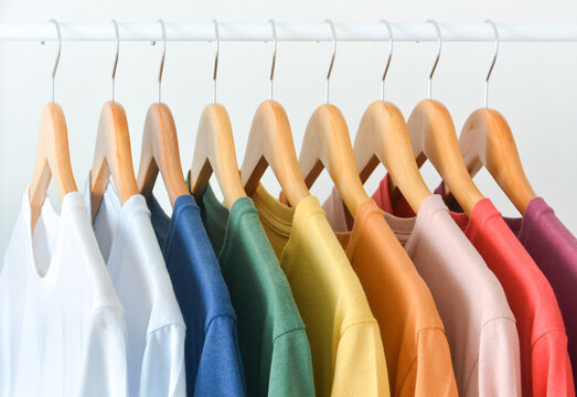 close up collection of pastel color t-shirts hanging on wooden clothes hanger in closet or clothing rack over white background