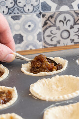 Man filling pastry with mincemeat to make mince pies.  In a metal baking tray on wood