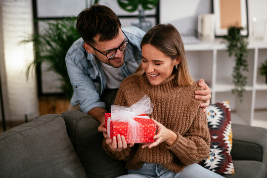 Boyfriend surprising his girlfriend with a gift. Young man giving a gift box to his girlfriend..