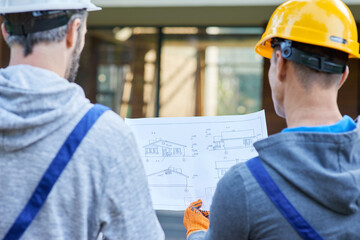 Plan better. Close up of two builders standing outdoors with an open blueprint discussing the...
