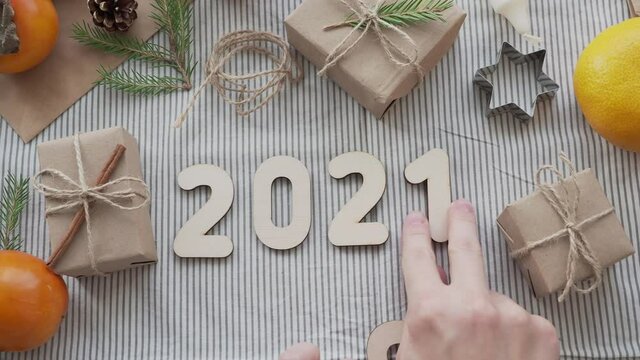 The numbers 2020 change to 2021 on the table among Christmas gifts, top view. Concept 2021 new year is coming. Girl in a sweater lays out 2021, Christmas holiday atmosphere.