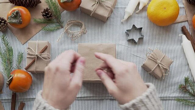The girl packs a Christmas gift in Kraft paper, ties a bow with a rope. Gifts for new year are handmade. Christmas atmosphere, gift packer's Desk.