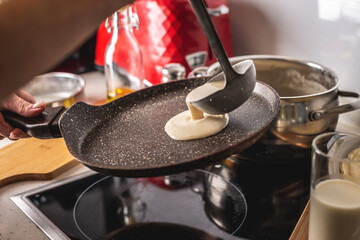 Person pouring the dough into a hot pan and frying homemade pancakes. Concept of making pancakes in your own kitchen