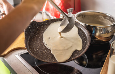 Person pouring the dough into a hot pan and frying homemade pancakes. Concept of making pancakes in...