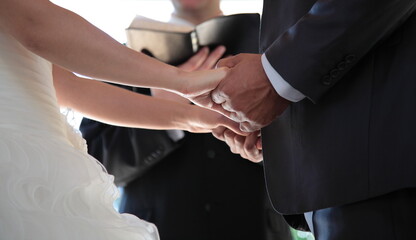 Obraz na płótnie Canvas View of a Groom and Bride hands holding together in front of the Priest holding a bible at a wedding Ceremony in Vancouver, British Columbia, Canada