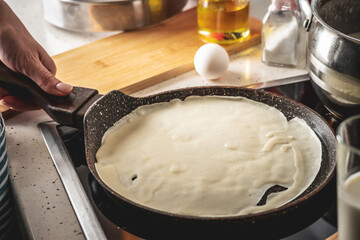 Person is standing at the stove and frying pancakes in a pan. Concept of the process of making a tasty breakfast at home