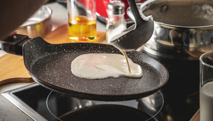 Person pouring the dough into a hot pan and frying homemade pancakes. Concept of making pancakes in...