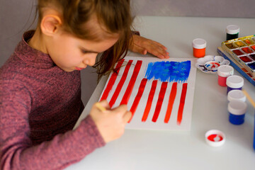Cute girl draws an American flag in watercolors. Patriotism, independence day, flag day concept.