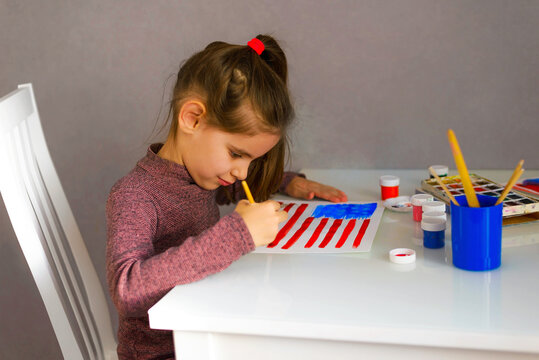 Cute girl draws an American flag in watercolors. Patriotism, independence day, flag day concept.