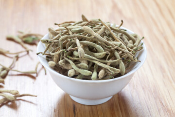 Dried honeysuckle in a ceramic cup on wooden table. Close-up.