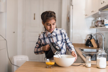 Fototapeta na wymiar Little girl use a mixer to make a cake, skilled girl in kitchen. Child trying making cookies.