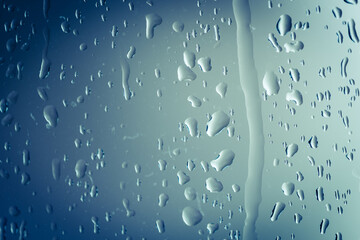 Close up of splashes of water and waterdrops running down on glass panel of bathtub in bathroom while taking a shower