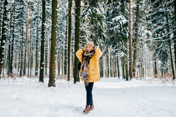 Young stylish hipster girl in yellow jacket with a warm scarf posing in the snow forest