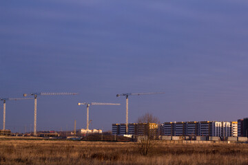Fototapeta na wymiar construction site with tower cranes in a field against a dark blue sky