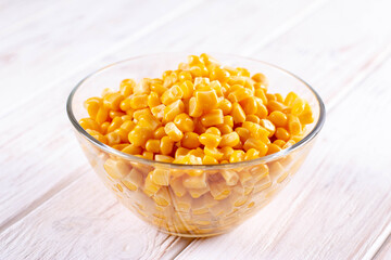 Canned sweet corn seeds in glass bowl on white wooden table