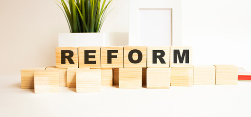 Wooden cubes with letters on a white table. The word is REFORM. White background.