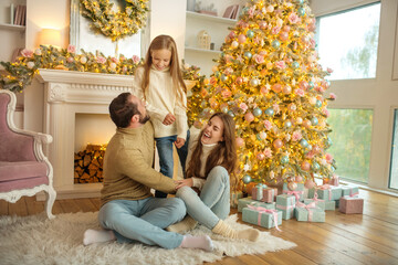Young family feeeling happy sitting near the new year tree
