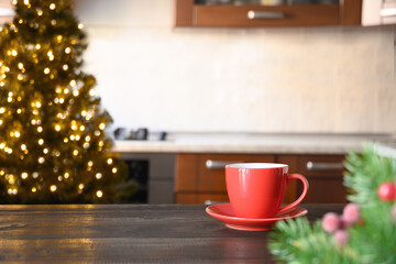 Fototapeta na wymiar Blurred Christmas kitchen with red cup of coffee on wooden tabletop. Background for design and montage. Find time for chill befor holidays.