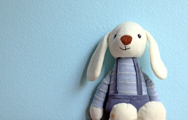 White rabbit toy is wearing blue striped overalls dress.  Children's toys sit and laying down with blue wall, friendly to young children and baby. Suitable for enhancing children's skills development.