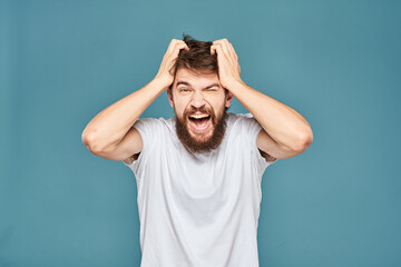 A bearded man in a white T-shirt gestures with his hands emotions blue background