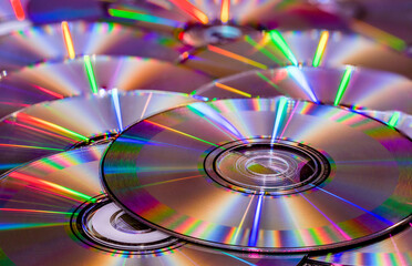 Close-up semi-abstract image of compact discs reflecting colorful lights and reflections, with shallow depth of field going to soft focus in the background.