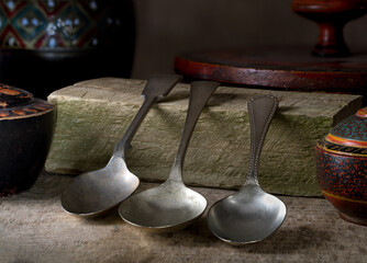 Close-up stylised still-life image of three vintage spoons set amongst a natural wood base with wooden artefacts, and directional lighting.