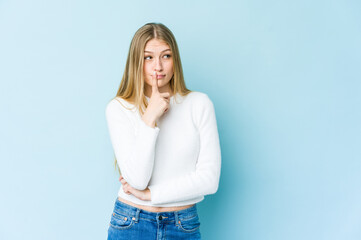 Young blonde woman isolated on blue background looking sideways with doubtful and skeptical expression.