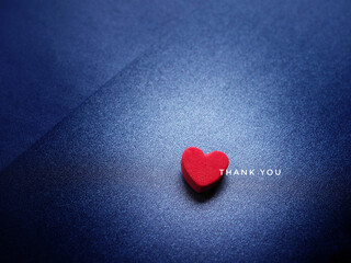 The word Thank You and red heart on glittering dark blue paper background.