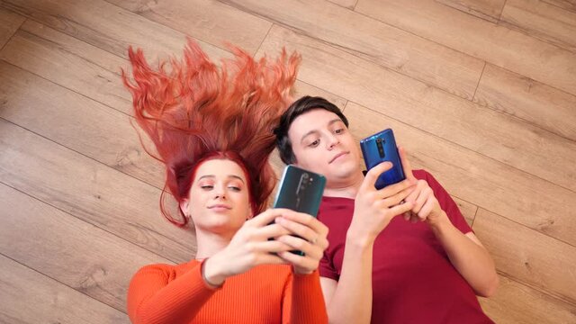 Young Guy and Girl Teenagers use Mobile Smart Phones lying on a Floor