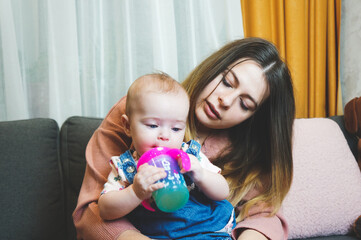 mom gives baby drink from sippy cup, maternal care concept, lifestyle