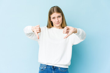 Young blonde woman isolated on blue background showing thumb down, disappointment concept.