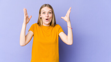 Young blonde woman isolated on purple background celebrating a victory or success, he is surprised and shocked.