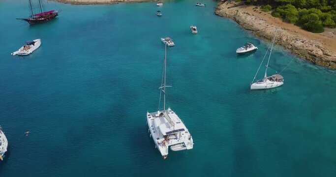 Revealing drone shot of moored catamaran and people diving into the sea near bay