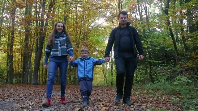 Family of three on a walk in autumn forest, parents and son playing, kid jumps