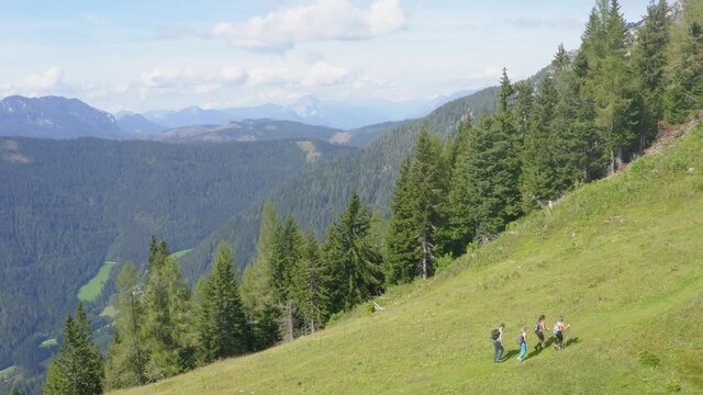 Four friends hiking on green mountain slope, Alps. Aerial backward