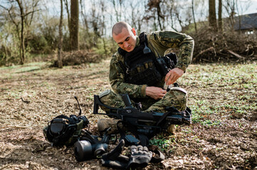 Soldier un Cropat uniform fixing his assault rifle G36 in the forest on a sunny day.