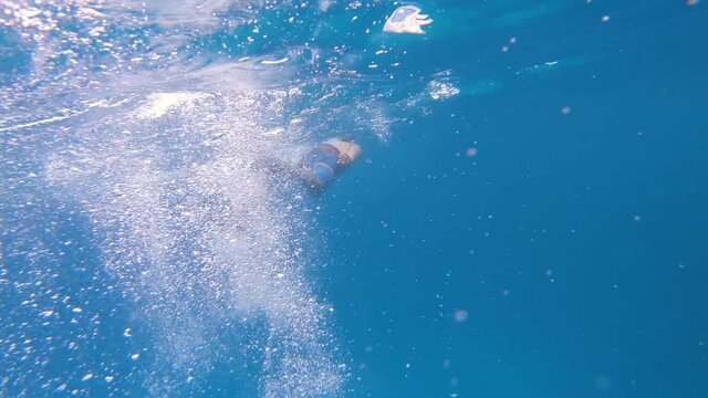 On a deep blue ocean of the Galapagos islands, a man is snorkeling and swimming using his flip flops which are creating bubbles because of the movement.