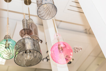 A group of switched-off multicolored lamps with a gray, turquoise, pink glass ceiling is suspended...
