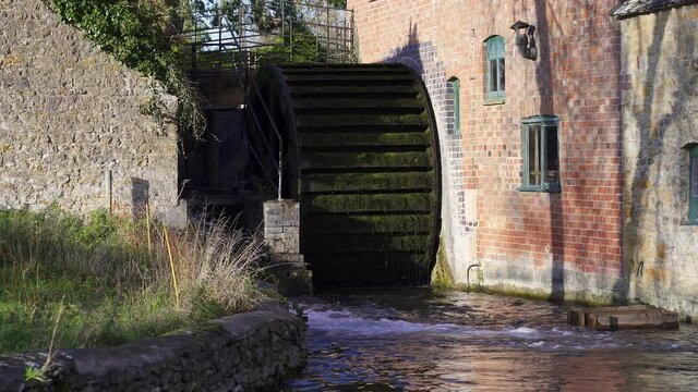 An old wooden undershot waterwheel on the side of a historic water mill in Lower Slaughter in the Cotswolds. Gloucestershire, England, UK