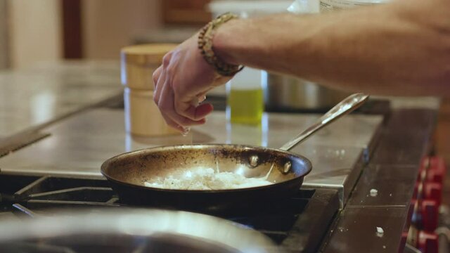 Man sprinkling handful of cheese over frying pan in slow motion
