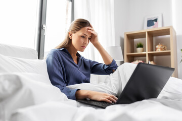 technology, internet and people concept - stressed young woman with laptop computer in bed at home bedroom