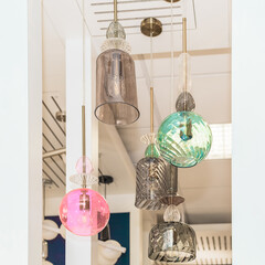 A group of switched-off multicolored lamps with a gray, turquoise, pink glass ceiling is suspended...