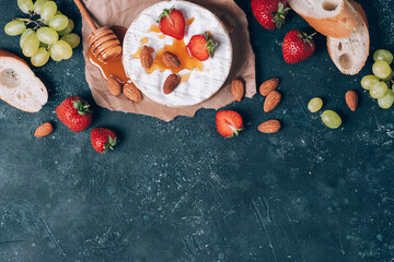 French camembert cheese served on grape, honey, almond, strawberries, baguette on dark background. Top view. Copy space. Romantic date night. Valentine's Day, love concept. Romantic dinner