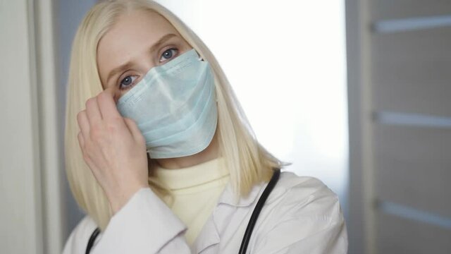 Portrait Of Overworked Nurse Taking Off Face Mask During Break In Busy Hospital During Health Pandemic