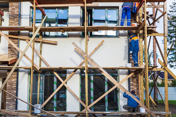Workers are painting the facade from wooden platform in house is under construction, remodeling,...