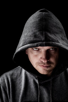 Dark low key portrait of a man looking at camera with a serious facial expression, wearing gray hood