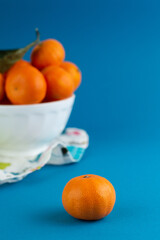 There is a plate of tangerines in the background and a tangerine in the foreground against a blue background.