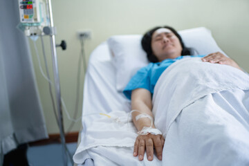 Obraz premium Close-up of a patient's hand, an Asian woman lying on a bed, giving a saline solution at a hospital