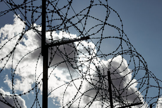 Black silhouette of barbed wire against a cloudy sky and sun
